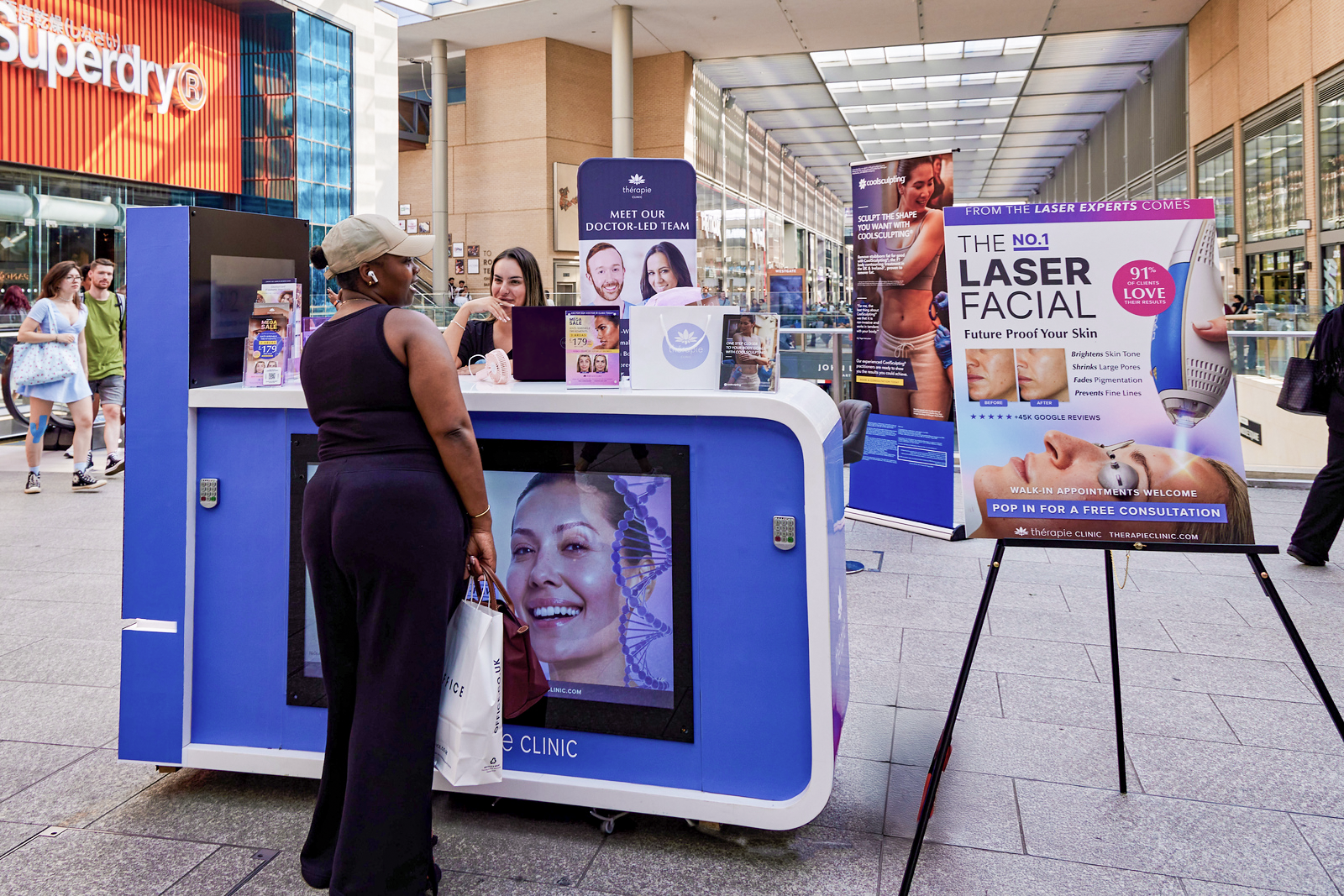 Thérapie Clinic customer acquisition event at Westgate Oxford shopping centre with branded promotional stand for aesthetics sign-ups.